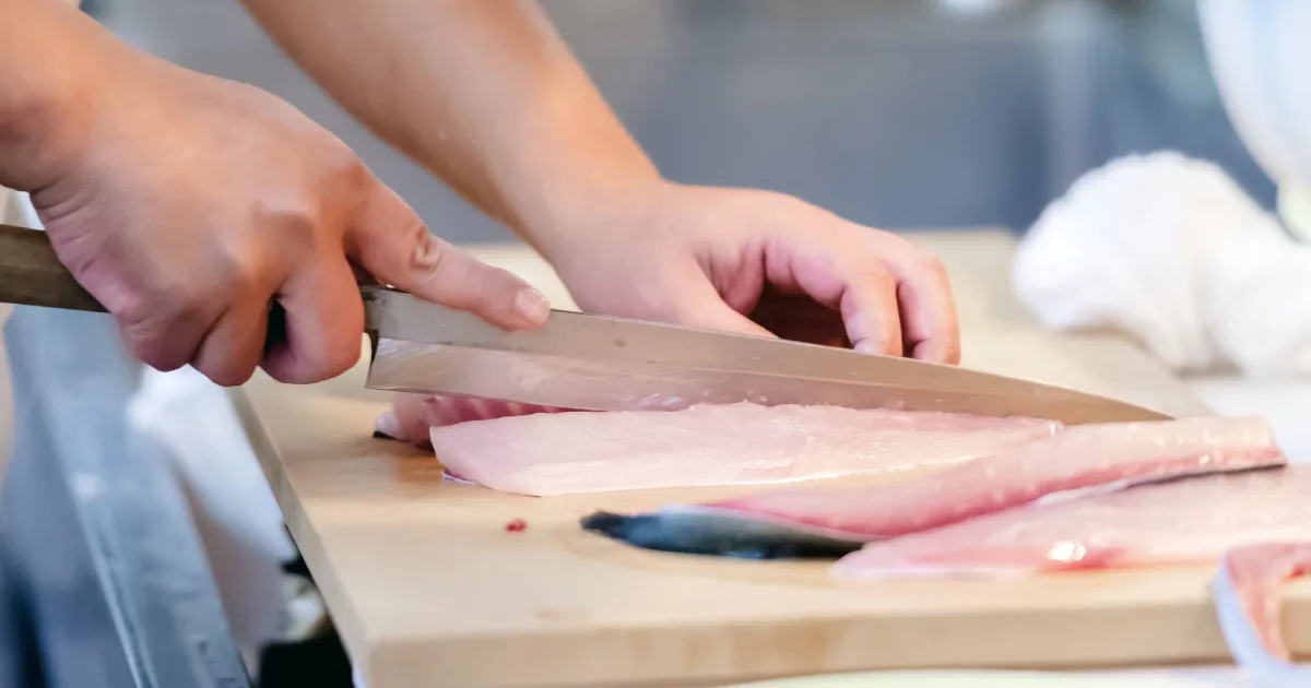 鮮魚加工の現場で魚を捌いている様子。包丁で丁寧に魚をフィレにしている作業風景。