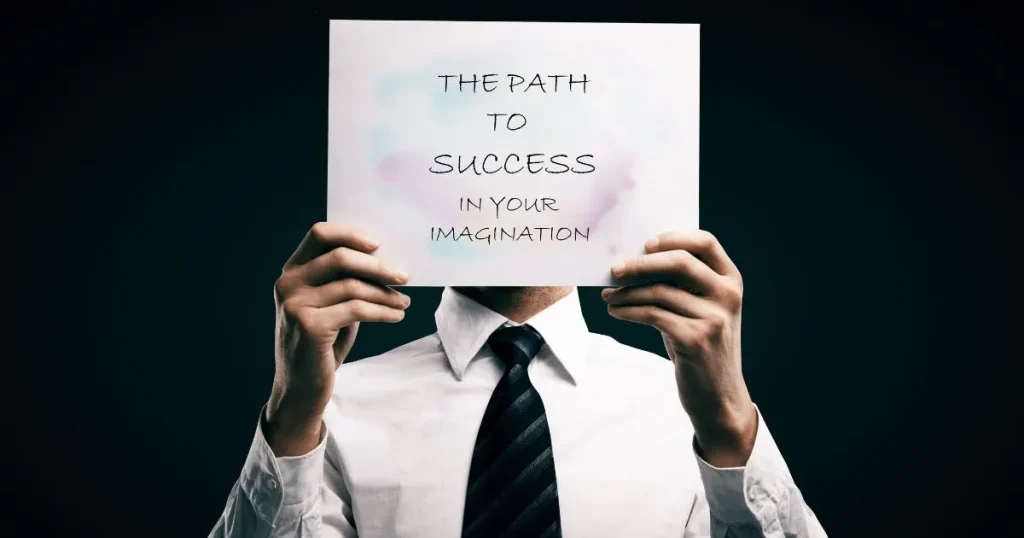 スーツを着た人物が「THE PATH TO SUCCESS IN YOUR IMAGINATION」と書かれた紙を顔の前に掲げている姿。就職活動でのモチベーションや成功への道を象徴するイメージ。