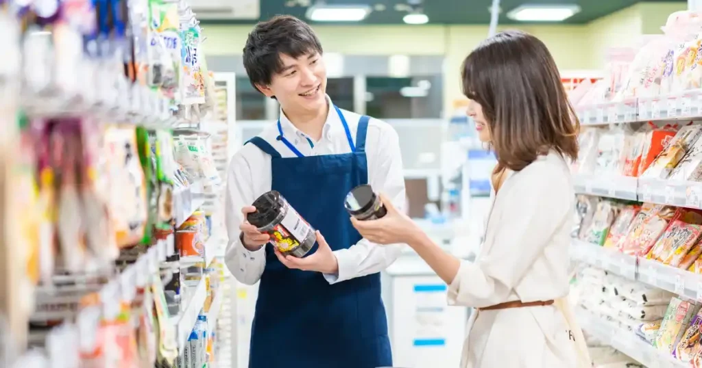 スーパーの店員が商品を手に取りながら女性客に説明している様子。