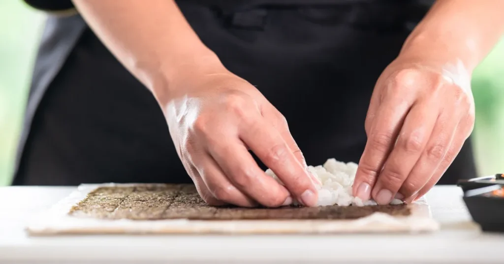 巻き寿司を作る寿司職人の手元。海苔の上にご飯を均等に広げる繊細な作業を行う修行中の風景。