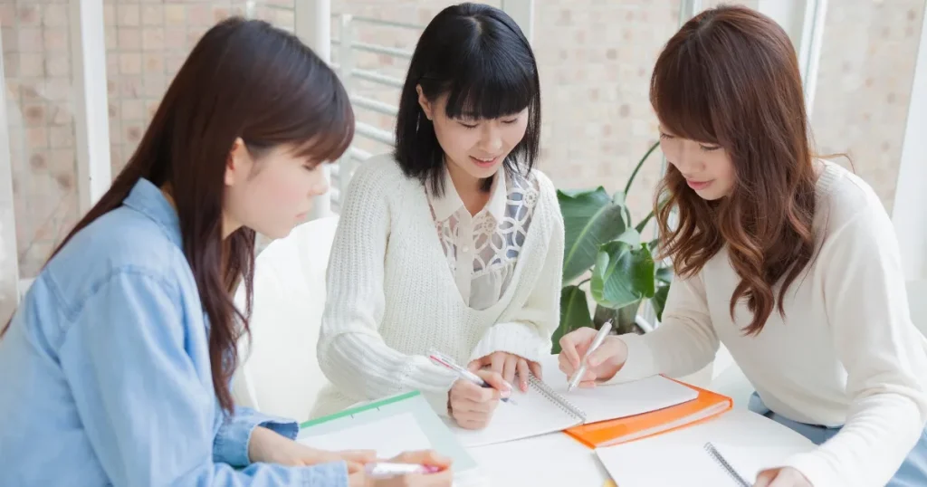 就活座談会後、ノートにメモを整理しながら情報を振り返る3人の学生。真剣な表情で話し合いをしている様子。