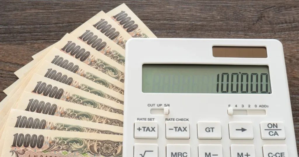 木製のテーブルに置かれた電卓と1万円札が並ぶ光景。転職活動中に利用できる公的支援や助成金を象徴するイメージ。