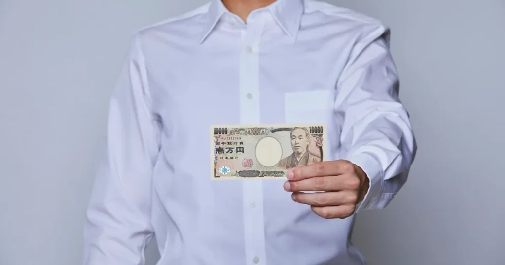 白いシャツを着た人物が1万円札を手に持っている姿。転職活動中にアルバイトやフリーランスで資金を補填する方法を象徴するイメージ。