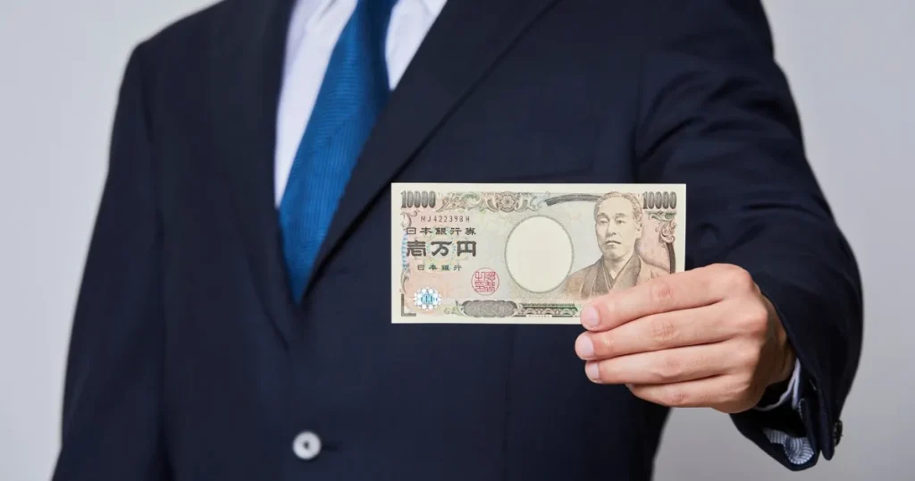 スーツを着た人物が1万円札を手に持ち、転職活動にかかる費用を象徴するイメージ。