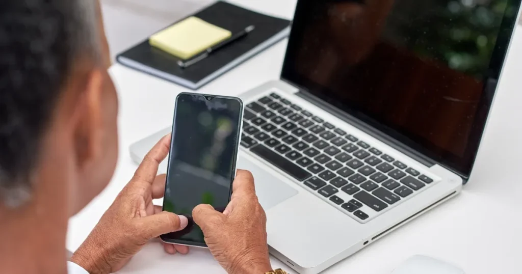 スマートフォンを操作する手元と開いたノートパソコン。50代転職の厳しさとデジタル対応への課題を象徴するイメージ。