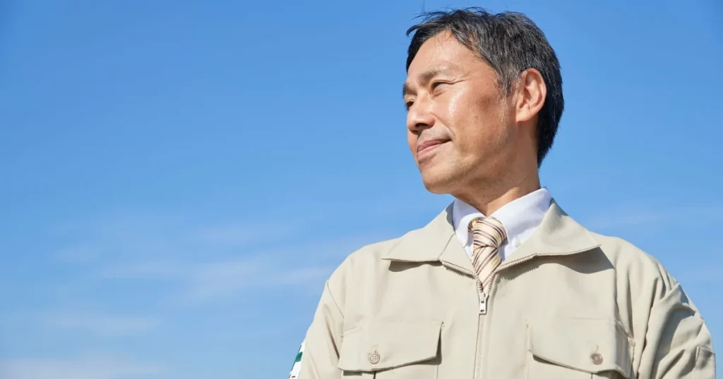 青空の下で前を見据える作業服姿の男性。50代転職の現状を象徴するビジュアル。