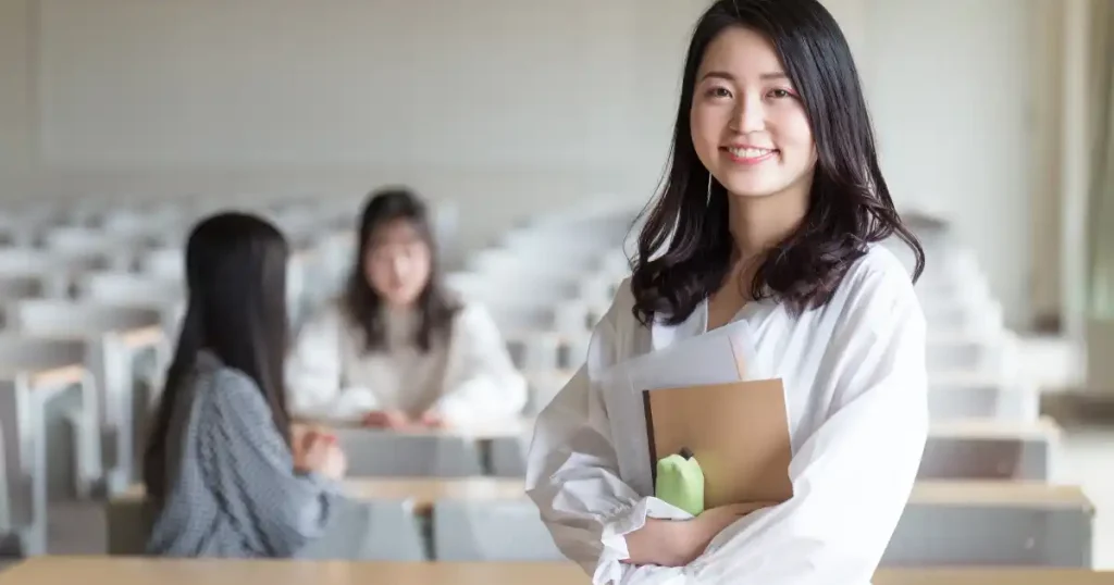 講義室で資料を持ちながら笑顔を見せる学生。IT業界就職を目指す文系学生の前向きな姿勢を象徴するイメージ。