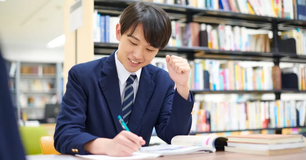 図書館で資料を見ながら就職イベントの準備を進めるスーツ姿の学生。真剣に取り組む様子。