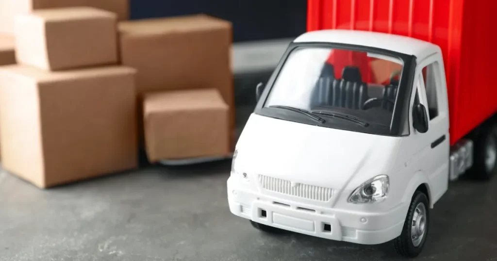 物流を象徴する小型トラックの模型と積み重ねられた段ボール箱。食品バイヤーの仕入れ・物流業務をイメージしたビジュアル。