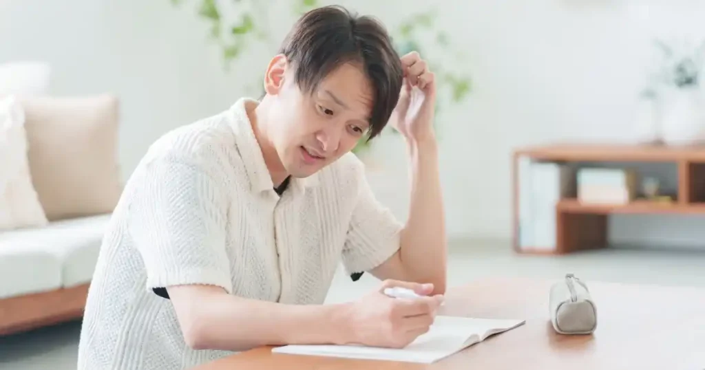 「退職タイミングを見極めるときのポイント【5つ】」について説明するセクションで使用されている画像。男性がノートに何かを書き込みながら頭を抱えて考えている様子。退職のタイミングについて悩んでいる状況を象徴しています。
