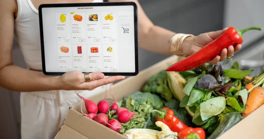 タブレットに表示されたオンライン食料品の注文画面と、新鮮な野菜が詰まった箱を手に持つ人物。ネットスーパーで必要なスキルや資格を象徴的に表現。