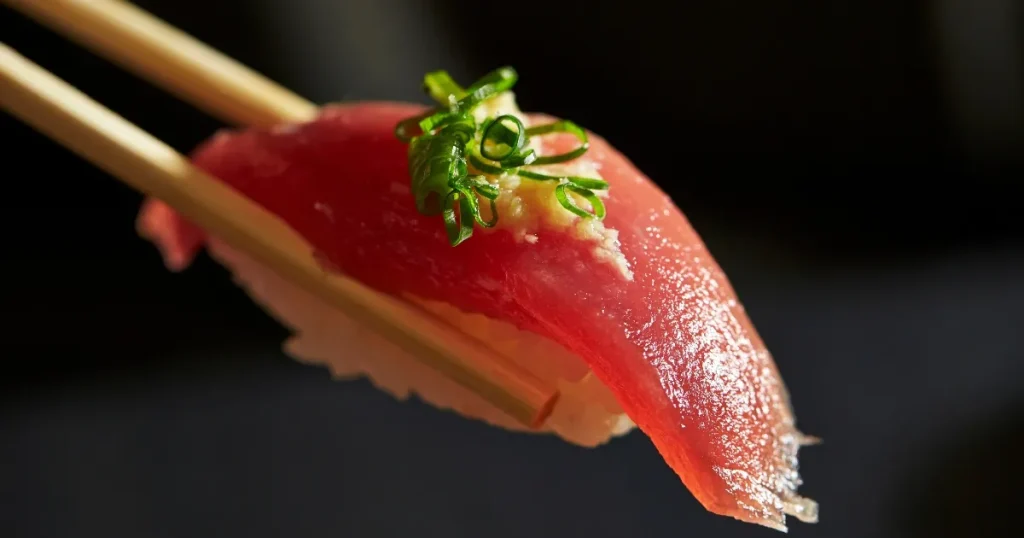 箸で持ち上げられた新鮮なマグロの握り寿司。寿司職人が生み出す一生使える職人技と日本食文化の魅力を象徴している。