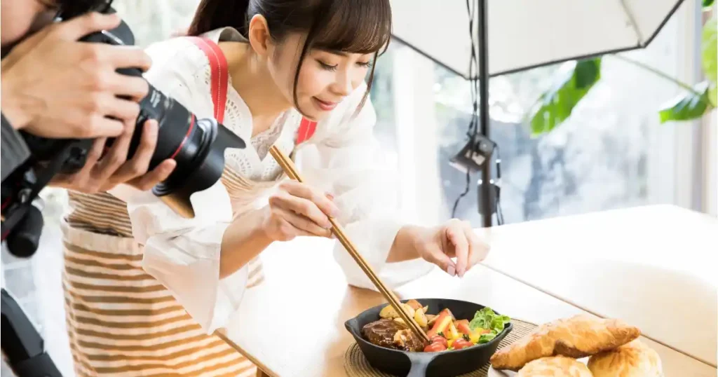 料理の盛り付けを行う女性と撮影するカメラマン：フードコーディネーターが料理の見た目を演出し、食の魅力を引き出している様子。