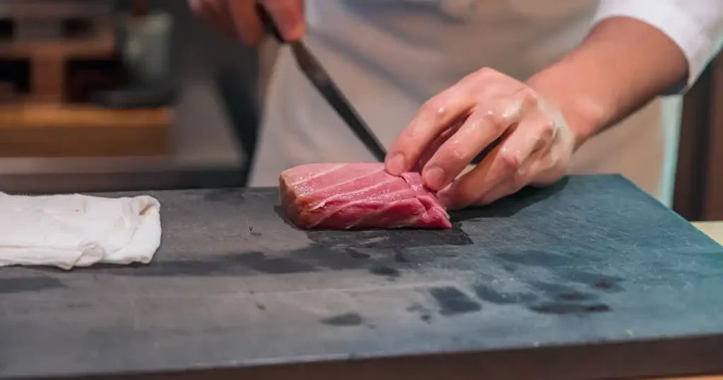 まな板の上で新鮮なマグロを丁寧に切り分ける料理人の手元。寿司職人と板前の技術の違いを象徴する場面。