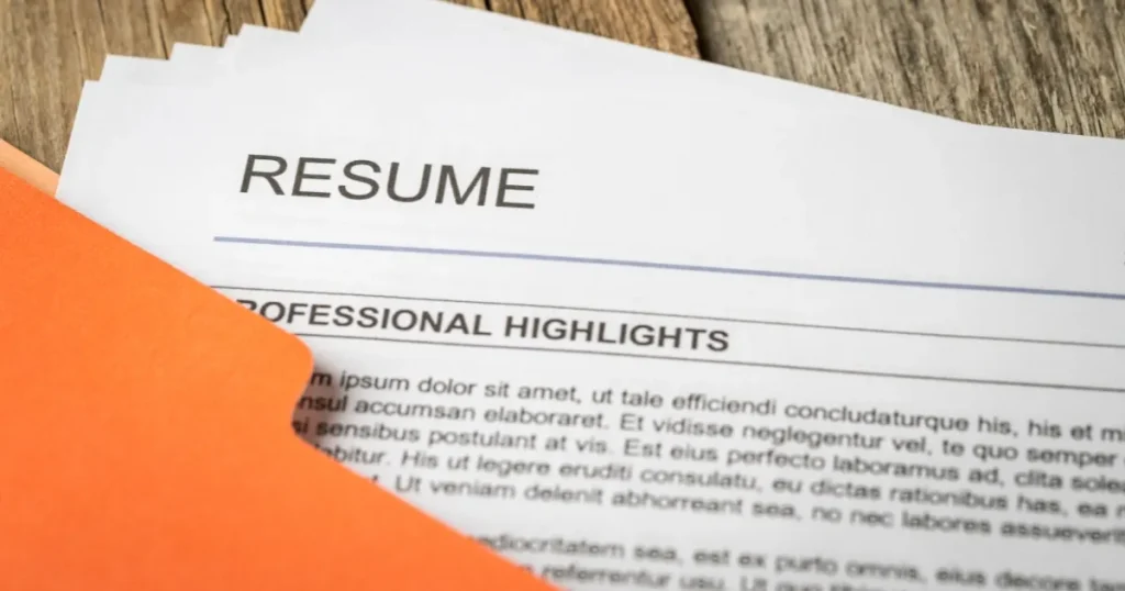 テーブルの上に置かれた履歴書（RESUME）とオレンジ色のフォルダー：志望動機の基本構成を解説するセクションを象徴するイメージ。