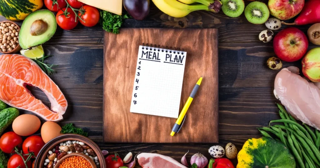 カラフルな食材と「MEAL PLAN」と書かれたノートが木製ボードに配置されている：フードコーディネーターになるために役立つ資格を象徴するイメージ。