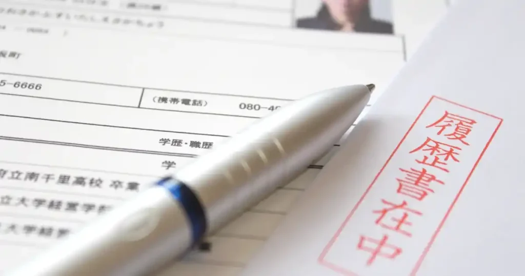 履歴書の上に置かれたボールペンと「履歴書在中」と記された封筒。転職活動における履歴書の重要性を象徴するイメージ。