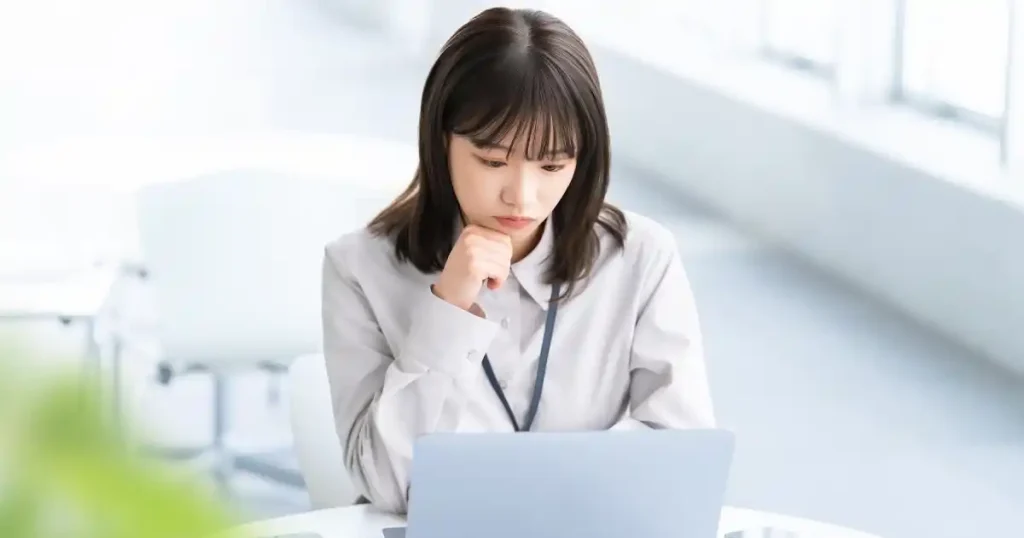 ノートパソコンを前に考え込む女性。履歴書が2枚になる場合の対処法やマナーについて調べている様子を象徴している。