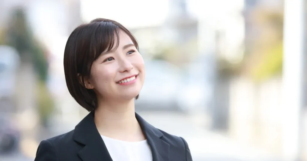 スーツを着た笑顔の女性が屋外で空を見上げている様子。第2新卒の求人情報でチェックすべきポイントを解説するセクションに関連したイメージ。