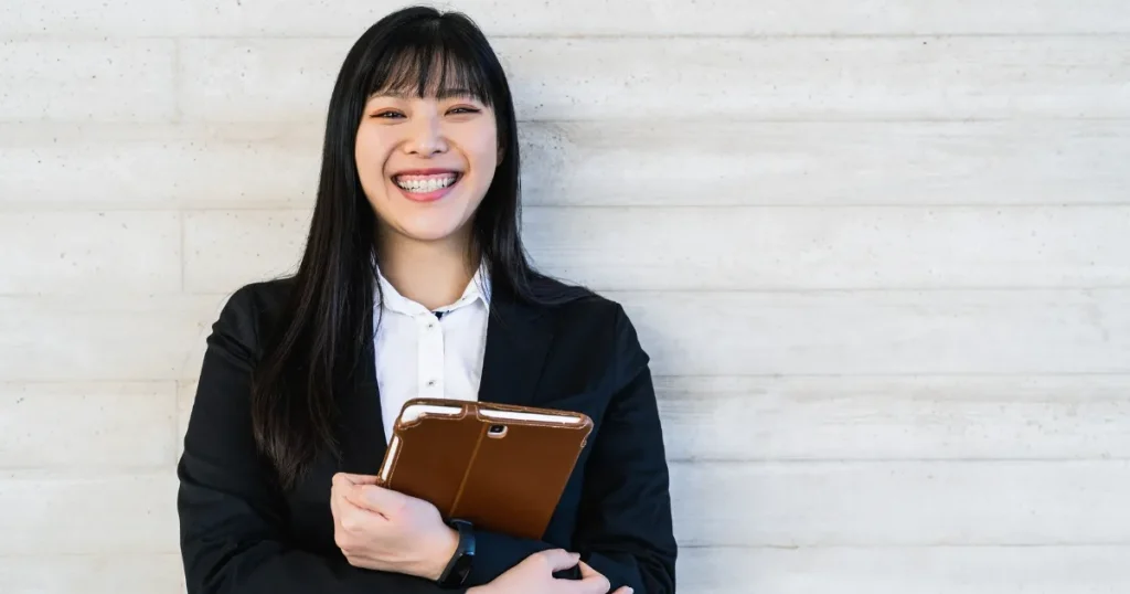 スーツを着た笑顔の女性がタブレットを抱えて立っている様子。第2新卒として転職を成功させるためのポイントを説明する場面を象徴。