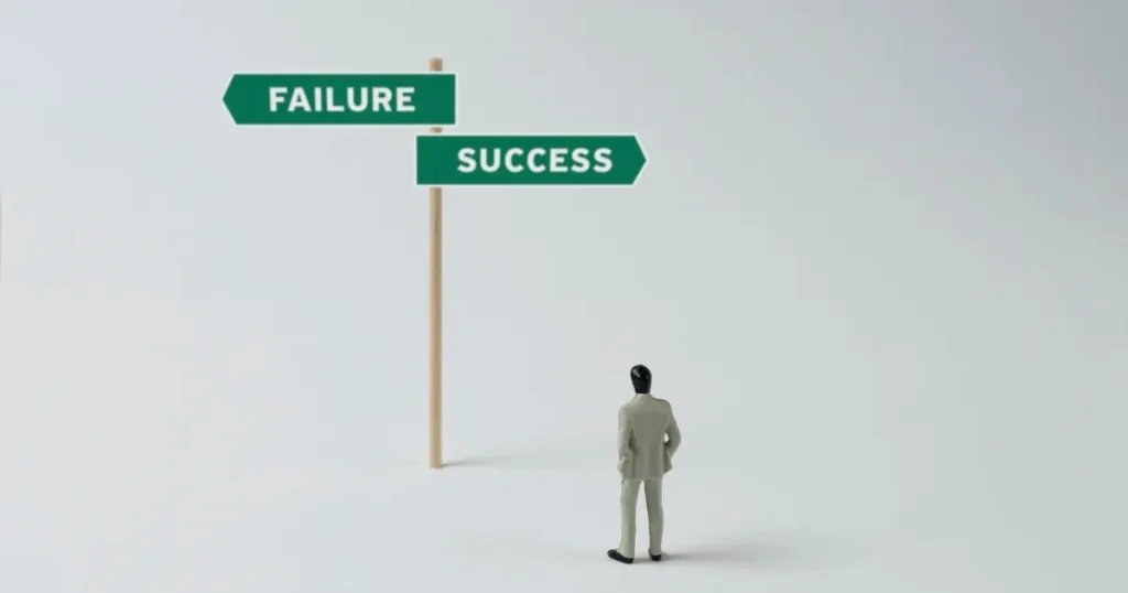 小さな人物のフィギュアが、左右に分かれた道標を見上げている。道標には「FAILURE（失敗）」と「SUCCESS（成功）」と書かれており、選択の重要性や転職の決断を象徴するイメージ。