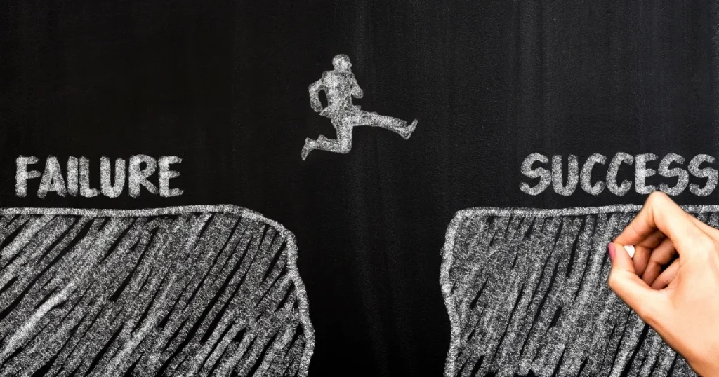 黒板に描かれた「FAILURE（失敗）」と「SUCCESS（成功）」の間を跳ぶ人物のイラスト。成功への挑戦や転職活動の準備を象徴するイメージ。