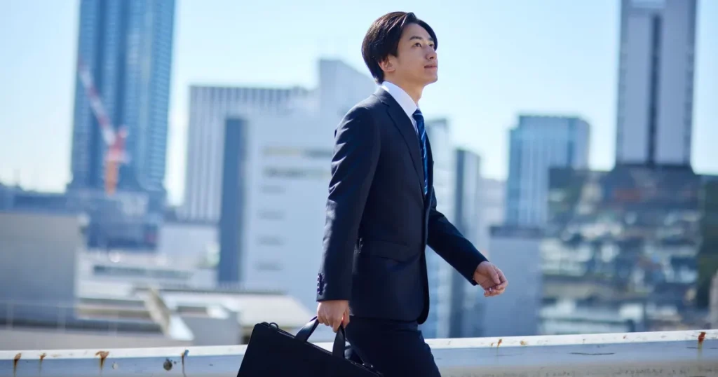 スーツを着た若い男性がビジネスバッグを持ちながら前を見据えて歩いている様子。都市の背景が広がり、キャリアを切り開く第二新卒の意気込みを象徴しています。
