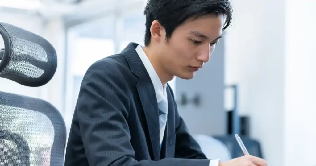 真剣な表情でメモを取るスーツ姿の男性。グロサリー部門のアルバイトにおける注意点に関連した姿勢や意識を象徴しています。