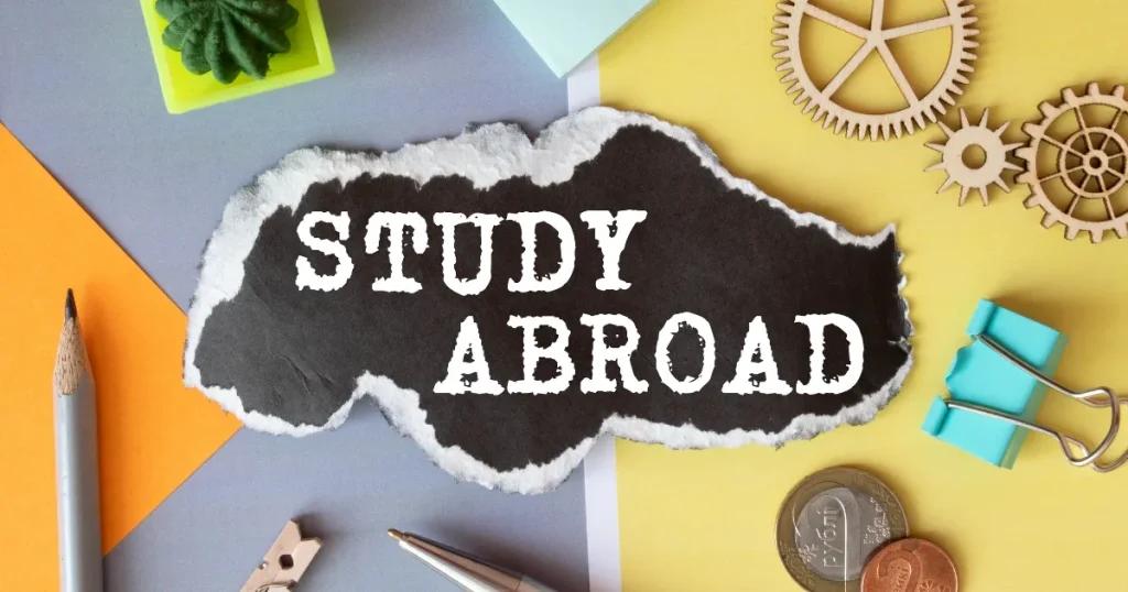 「STUDY ABROAD」と書かれた黒い紙が中央に配置され、周囲にペン、コイン、ギア型の装飾、クリップなどが散りばめられたデザイン。