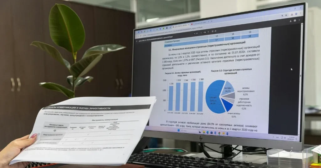 コンピューターの画面に表示されたグラフや円グラフと、それを手に持つ紙の資料を確認している場面。データ分析を通じての自己理解を象徴するイメージ。