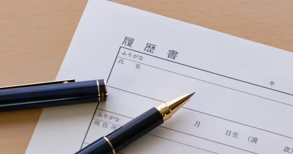 机の上に置かれた履歴書とペン。履歴書の一部が見え、名前や住所を記入する欄が確認できる。