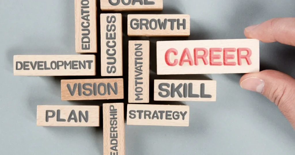 複数の木製ブロックに「CAREER」「SKILL」「VISION」「STRATEGY」などのキーワードが書かれており、キャリア形成の要素が描かれている。右側に手がブロックを動かしている様子。