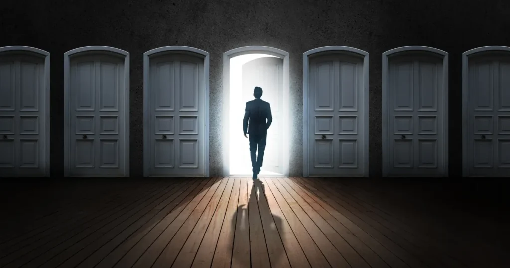 暗い部屋に並ぶ複数のドアの中から、光が差し込むドアを選び前進するスーツ姿の男性。ハイキャリア転職による新たなチャンスと可能性を象徴するイメージ。