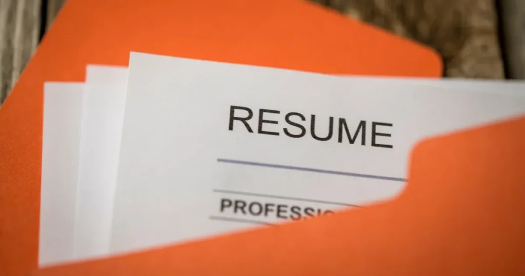 オレンジ色のフォルダーに収められた履歴書の一部が見えている。「RESUME」と記載され、履歴書の作成や提出に関連した内容を象徴している。