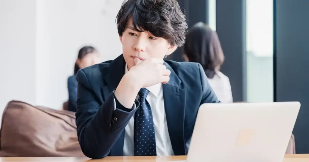 インターンシップ選びに悩む就活生|パソコンを前に考え込むスーツ姿の男性、選択ミスへの不安を象徴
