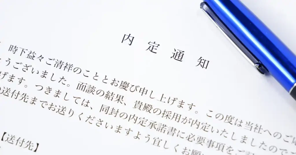内定通知書と青いボールペンの写真。内定後の具体的な準備事項や、入社前にやるべきことを10個に分けて解説するセクションで使用されている画像。