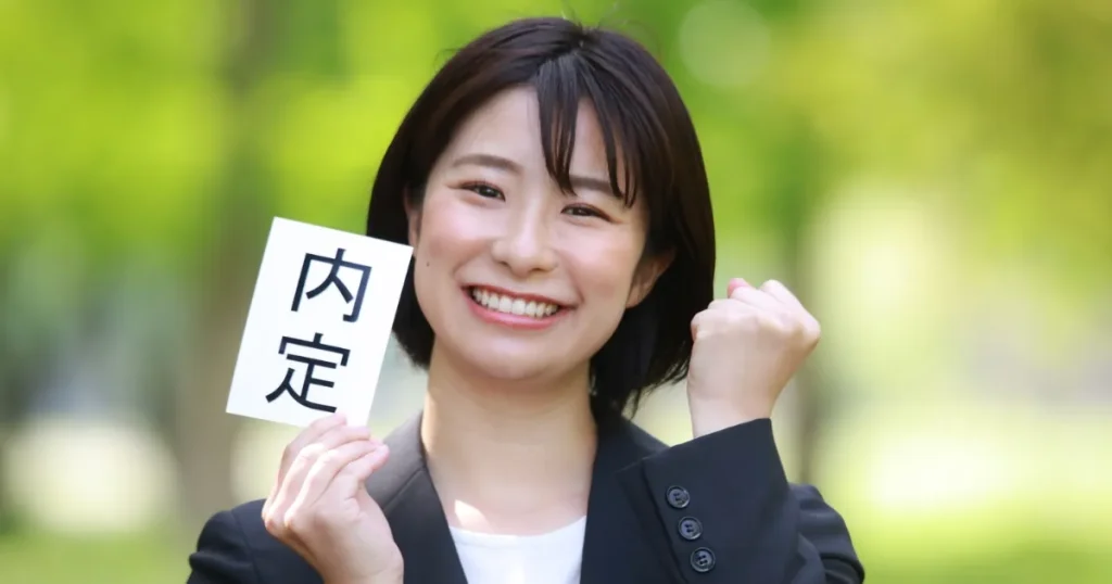 内定通知を手に笑顔を見せる就活生の女性。内定後の流れや社会人としての第一歩に向けた準備について解説する「一般的な内定後の流れ」セクションで使用されている画像。