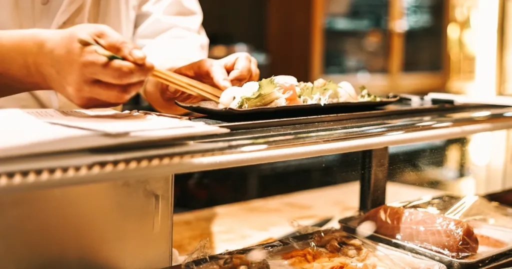 寿司職人が寿司を盛り付けている様子。カウンター越しに新鮮な食材が並び、職人の丁寧な手仕事が感じられるシーン。