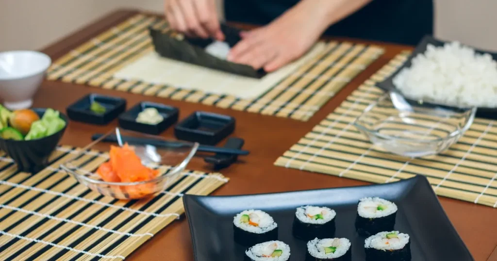 巻き寿司を作る寿司職人の手元。テーブルには完成した巻き寿司や食材が並び、丁寧な調理風景が広がる。