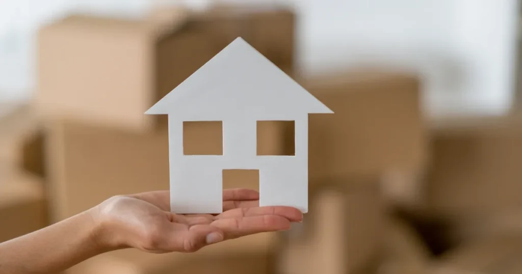 「新卒の引っ越し費用を抑えるためのポイントを解説するセクション。手に持たれた家のシルエットと背景に積まれた段ボールが新生活の準備を象徴。