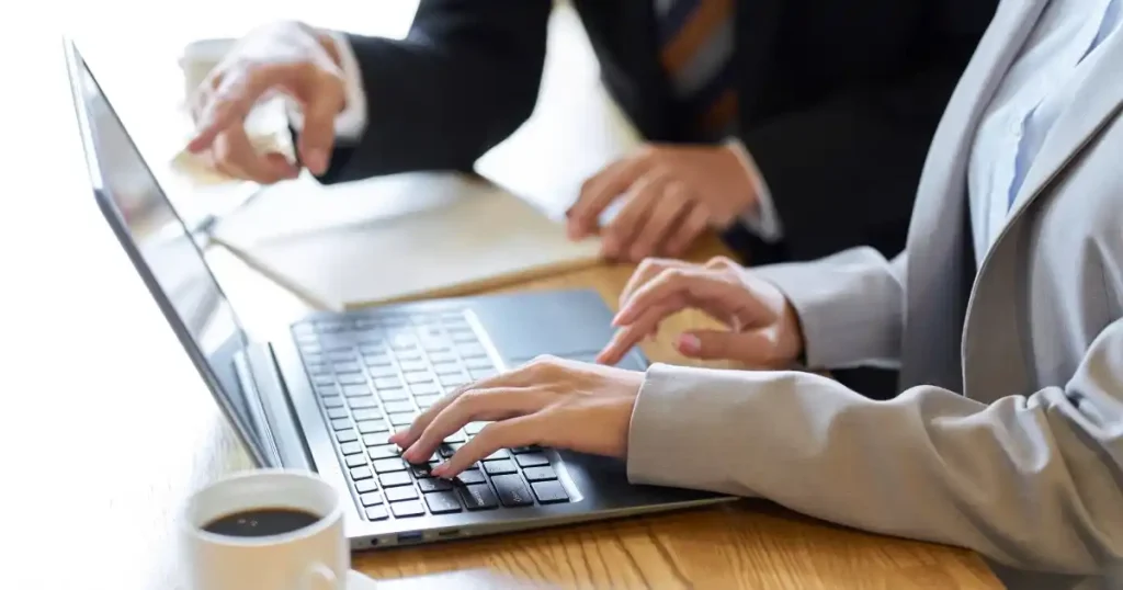 ノートパソコンを操作するスーツ姿の人物と、後ろからアドバイスをするもう一人の人物。キャリアコーチングが向いている人の特徴を解説するセクションに関連。