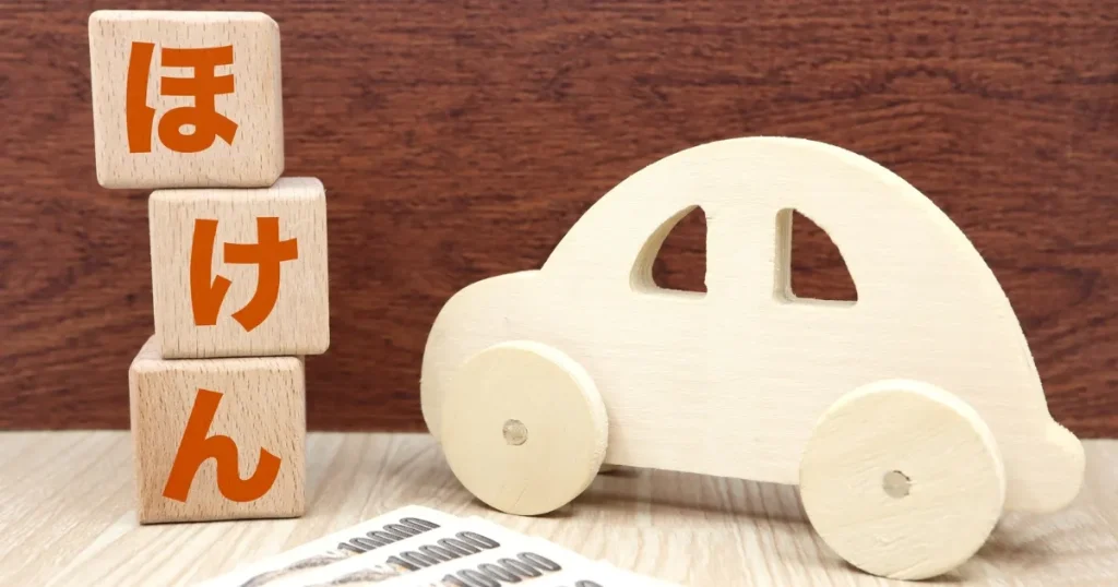 木製の車と積み木で『ほけん』と書かれたデザインイメージ。保険会社が扱うリスク保障やサービス内容を象徴するビジュアル。