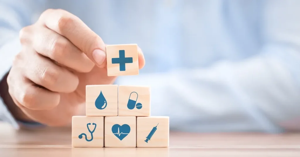医療や健康を象徴するアイコンが描かれた積み木を手で積み上げる様子。保険会社で必要な知識やスキルを視覚的に表現したイメージ。