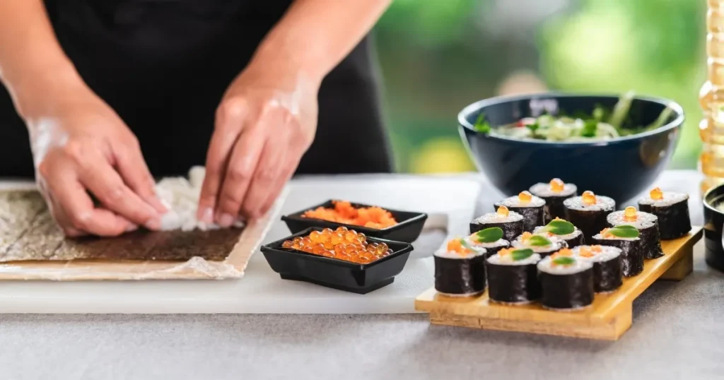 寿司職人が巻き寿司を丁寧に仕上げる様子。新鮮な具材や巻き寿司が並べられた調理台で、寿司職人として10年後も活躍するためのスキルと取り組みを象徴するイメージ。