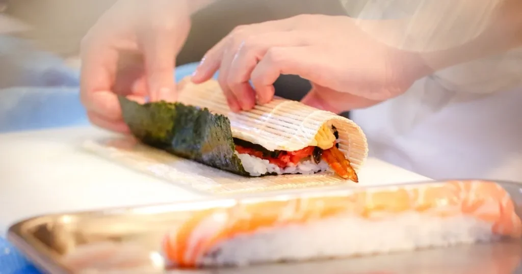 寿司職人が巻き簾を使って巻き寿司を丁寧に仕上げている様子。寿司職人業界の将来性を左右する要因を象徴するイメージ。