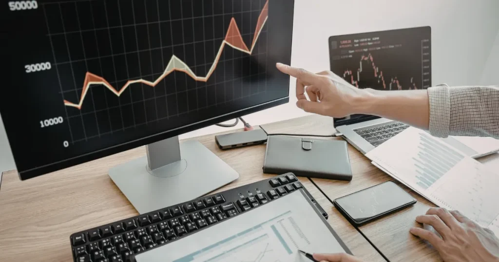 パソコン画面に表示されたデータ分析のグラフを指し示しながら議論する場面。自己分析の重要性を解説するセクションを象徴したイメージ。