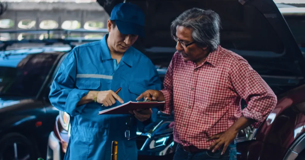 外国人自動車整備士が顧客と作業内容を確認している様子。日本で働く際の注意点や職場文化について解説するセクションに関連。