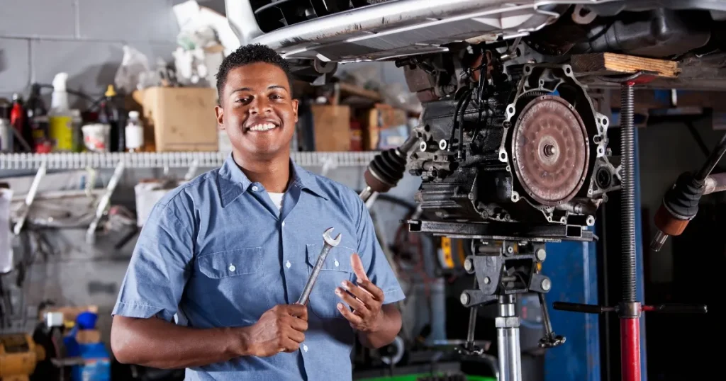 エンジン整備中に笑顔を見せる外国人自動車整備士。日本で働く外国人整備士が得られるメリットについて解説するセクションに関連。