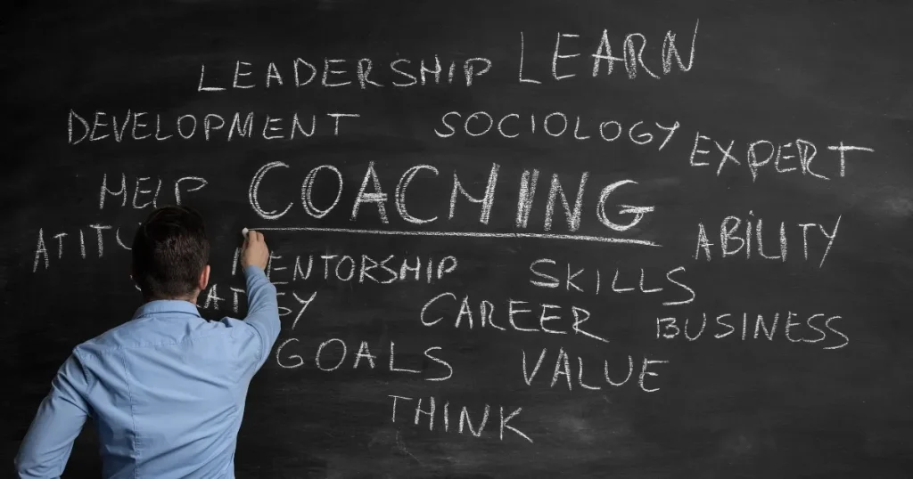 黒板に「COACHING」を中心に「リーダーシップ」「スキル」「価値」「ゴール」などの関連キーワードを書き込む人物。転職でキャリアコーチングを利用する際のデメリットを解説するセクションに関連。