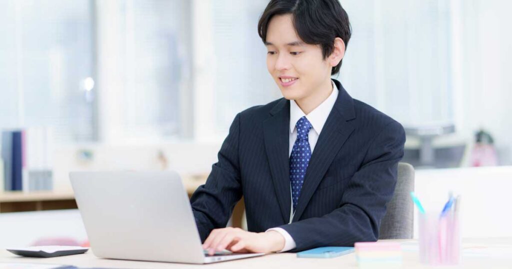 スーツ姿の男性がノートパソコンに向かいながら作業中。転職の問い合わせ方法として、メールが適切な選択肢であることを象徴するシーン。